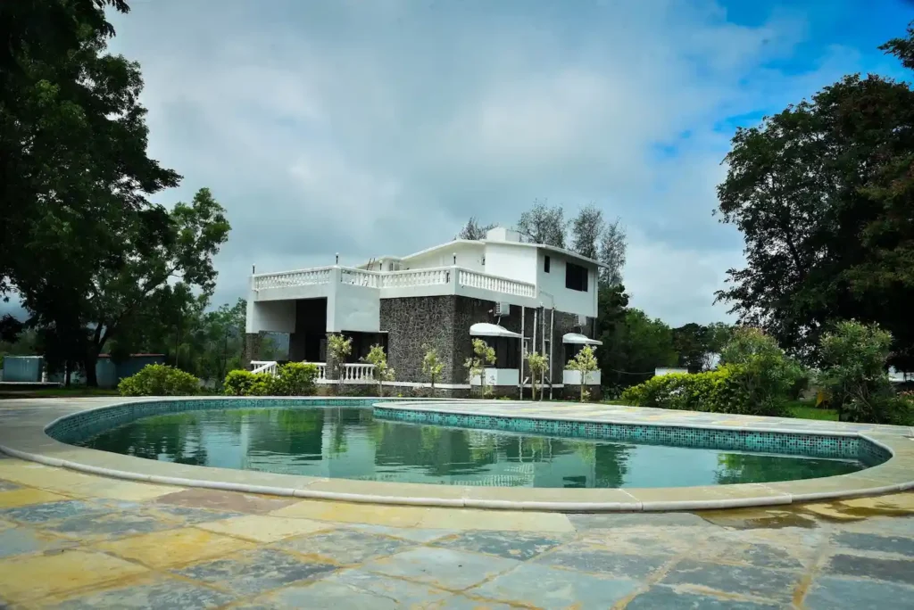 Private pool with lounge chairs and green hill views at Whispering Woods Farmhouse Naugaon